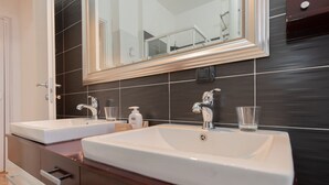 Baño con dos lavabos, un espejo y una pared de azulejos oscuros.