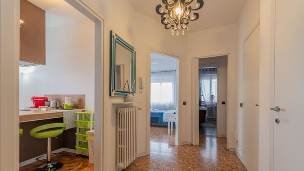Un pasillo con una zona de cocina a la izquierda, un radiador y una puerta que da a otra habitación.