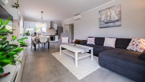 Een moderne woonkamer met een donkere bank, een witte salontafel en een schilderij van zeilboten.