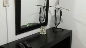 Una consola negra con un espejo encima, un control remoto y un frasco decorativo pequeño sobre la mesa.
