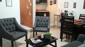 Una sala de estar con dos sillones, una mesa de centro con revistas, una planta pequeña y un comedor con una mesa y sillas.