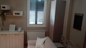 A room with a radiator, a window with blinds, a white sofa, a cabinet with storage boxes, and a sign labeled 'KITCHEN NOTES'.