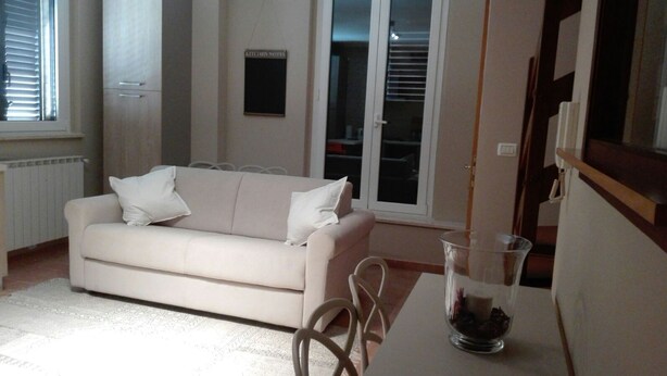 A living room with a beige sofa, a glass coffee table, and a chair. There is a sign on the wall that reads "KITCHEN NOTES".