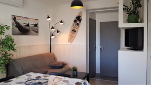 Una sala de estar moderna con un sofá, una mesa de centro con mantel estampado, una lámpara de pie, una decoración de tabla de surf y un televisor sobre un mueble.
