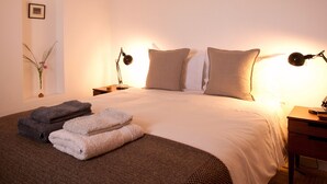 Un lit bien fait, avec des oreillers et des serviettes pliées, une table de chevet avec une lampe et un cadre photo fixé au mur.