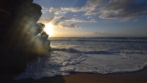 Une plage avec des vagues, une formation rocheuse et le soleil se couchant ou se levant.