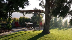 Une terrasse avec une table et des chaises en bois, entourée d’arbres et d’une pelouse verdoyante.