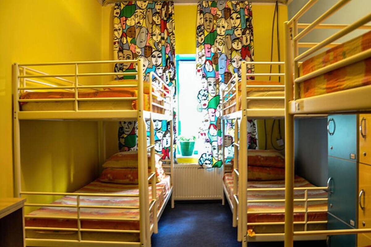 A dormitory room with bunk beds, a radiator, and a curtain with a colorful pattern.