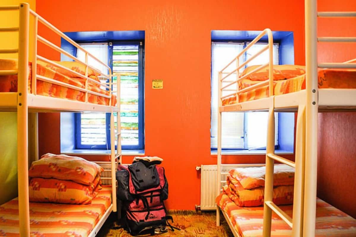 A dormitory room with bunk beds, a radiator, and a window with blinds.