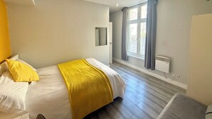 A bedroom with a bed, a window with curtains, a radiator, and a wall-mounted mirror. - King’s Cross Apartment Ground floor  (London)