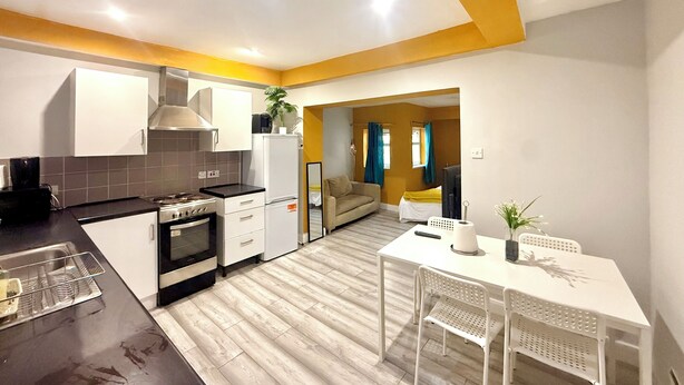 A compact kitchen with modern appliances, a dining area with a white table and chairs, and a living space with a sofa and curtains. - King’s Cross Apartment Ground floor  (London)