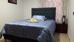 A bedroom with a bed, a nightstand, a wall-mounted painting, and a patterned curtain.