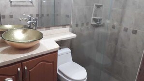 A bathroom with a glass shower enclosure, a white toilet, and a glass bowl sink.