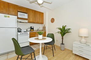 A compact kitchen with wooden cabinets, a white refrigerator, a microwave, a stove, and a small dining table with two chairs.