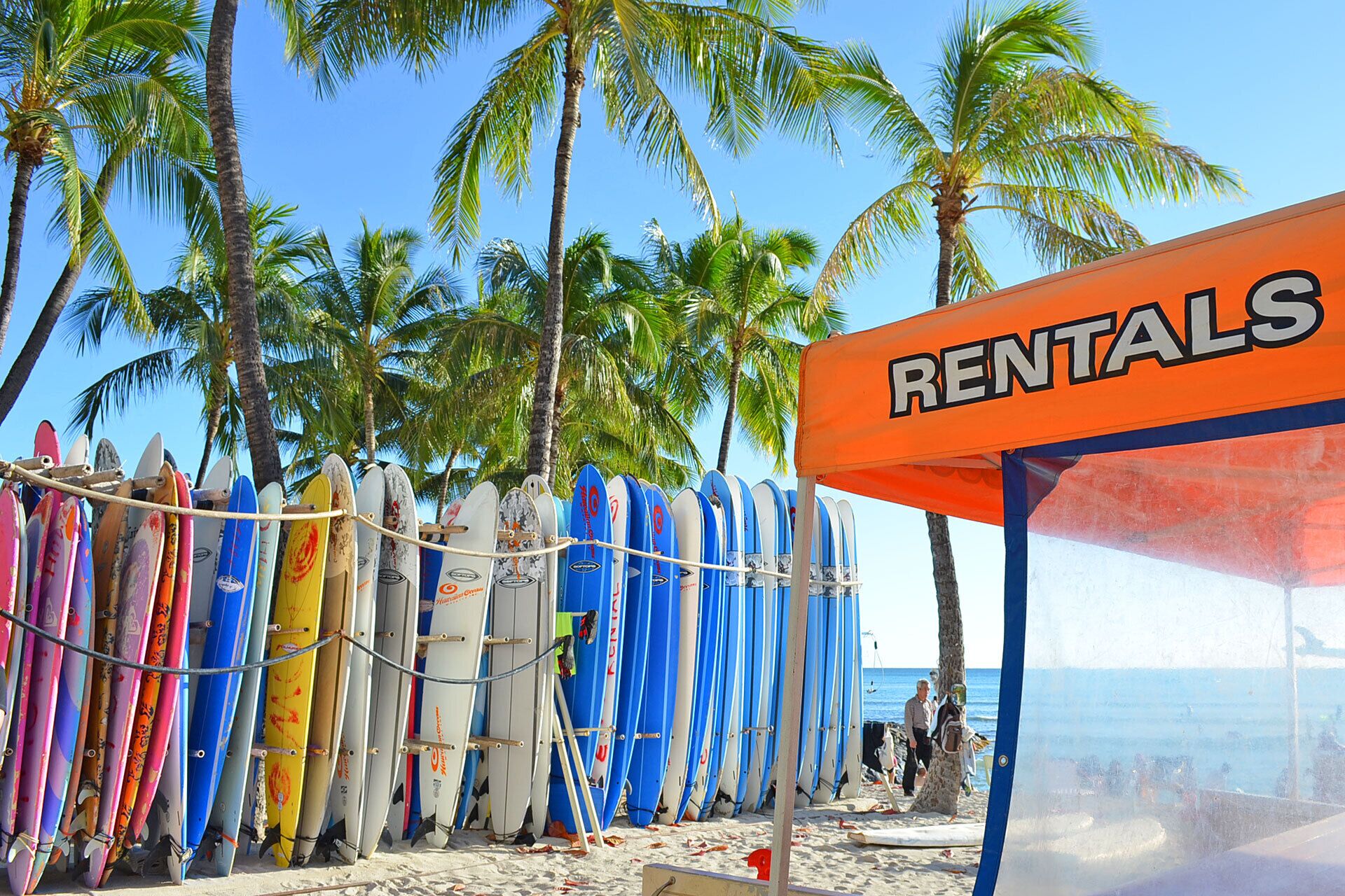 Une zone de location sur la plage où l’on peut louer des planches de surf, avec un panneau indiquant « LOCATION ».