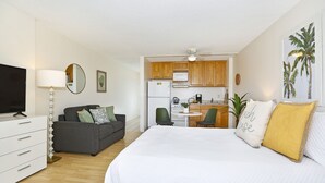 A compact hotel room with a bed, a TV, a desk, and a kitchenette. - 25th Floor Ocean Views! AC, Washer/Dryer, Wi-Fi, Rooftop Pool, FREE Parking! (Honolulu)