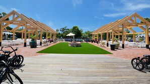 Una terraza de madera con un área central cubierta de césped y una estructura tipo pabellón.