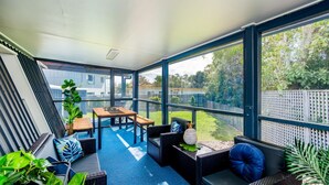A sunlit room with a large window, a wooden table, and wicker furniture. - Wayfarers Beachouse - Rainbow Beach. Everything you need, just metres to the beach. Pets welcome (Rainbow Beach)