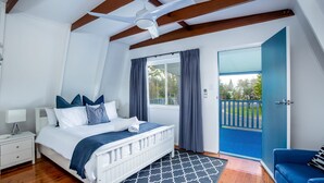 A bedroom with a bed, a nightstand, a ceiling fan, a window with curtains, and a view of the outside. - Wayfarers Beachouse - Rainbow Beach. Everything you need, just metres to the beach. Pets welcome (Rainbow Beach)