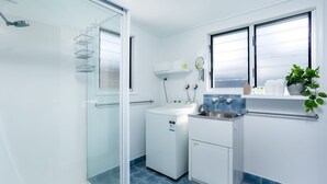 A compact kitchen with a washing machine, a sink, and a window with blinds. - Wayfarers Beachouse - Rainbow Beach. Everything you need, just metres to the beach. Pets welcome (Rainbow Beach)