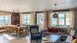 Ein geräumiges Wohnzimmer mit einem Holzessttisch, bequemen Sitzgelegenheiten und großen Fenstern mit Blick ins Freie.