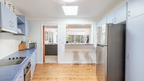 Una cocina moderna con estufa integrada, microondas y refrigerador. Hay dos taburetes y una ventana con vista a un jardín.