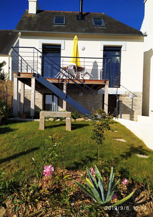 Une maison à deux étages avec un balcon, un escalier et un parapluie jaune.