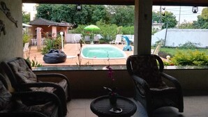 A covered patio with wicker furniture, a small table with a vase, and a view of a swimming pool and outdoor seating area. - House on Itaparica Island - Ponta de Areia Beach (Itaparica)