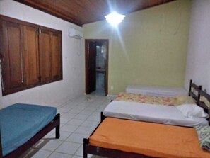 A room with two beds, one with an orange mattress and the other with a blue mattress. There is a wooden wardrobe and a door leading to another room. - House on Itaparica Island - Ponta de Areia Beach (Itaparica)