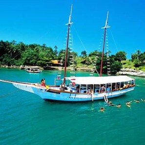 A traditional boat with passengers, surrounded by calm turquoise waters and lush greenery. - House on Itaparica Island - Ponta de Areia Beach (Itaparica)