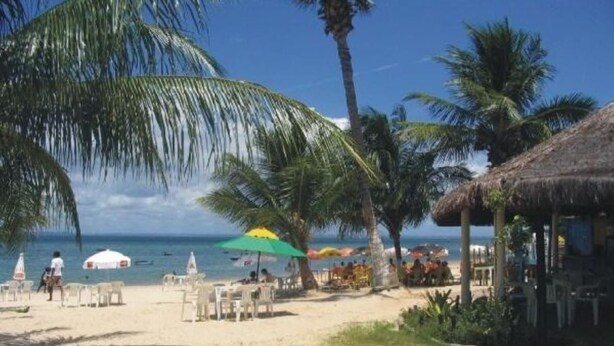 A beach with palm trees, beach chairs, umbrellas, and a thatched-roof structure. - House on Itaparica Island - Ponta de Areia Beach (Itaparica)