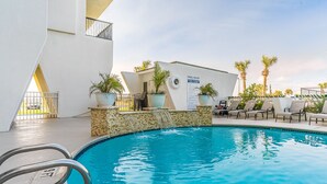 A swimming pool with lounge chairs and potted plants, surrounded by a white building with a poolside area. - Sunny beachfront condo (Galveston)