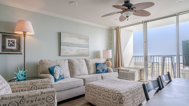 A cozy living room with a beige sofa, ottoman, and chairs, a dining table, and a large window offering a view of the ocean. - Sunny beachfront condo (Galveston)