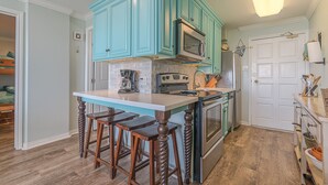 A kitchen with teal cabinets, a central island with stools, a microwave, oven, and a sink. - Sunny beachfront condo (Galveston)