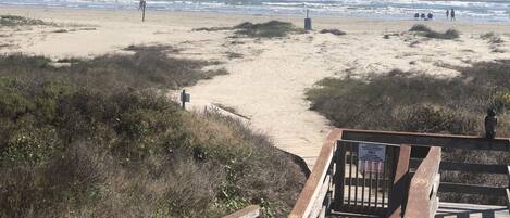 A wooden boardwalk leading to a sandy beach with ocean views.