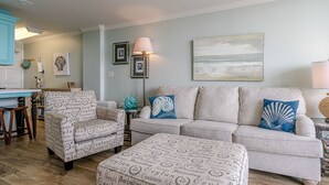 A living room with a sofa, armchair, ottoman, and a lamp. - Sunny beachfront condo (Galveston)