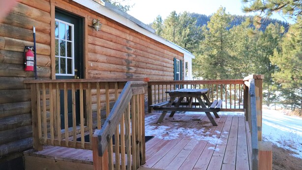 A wooden cabin with a deck, a fire extinguisher, and a picnic table.