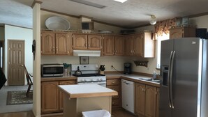 A kitchen with wooden cabinets, a stainless steel refrigerator, a microwave, a stove, and a trash can.
