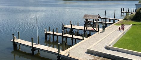 A wooden dock extending into a calm body of water, with a grassy area and a small structure on the right.