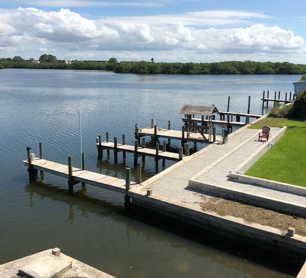 A wooden dock extending into a calm body of water, with a grassy area and a small structure on the right.