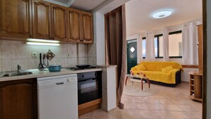 Une cuisine avec des meubles en bois, un lave-vaisselle, un four et une cuisinière. Le salon est doté d’un canapé jaune et offre une vue sur l’extérieur.