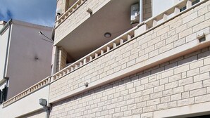 Un immeuble de deux étages avec une façade en briques, une voiture bleue garée devant et un escalier menant à l’étage supérieur.