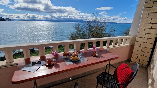 Un balcon avec une table dressée pour un repas, donnant sur une étendue d’eau et sur une terre lointaine.