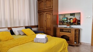 Une chambre à coucher avec un lit, une armoire en bois, un téléviseur et un tableau accroché au mur.