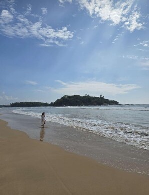 Una playa con una persona caminando por la orilla, una isla distante y un cielo despejado.