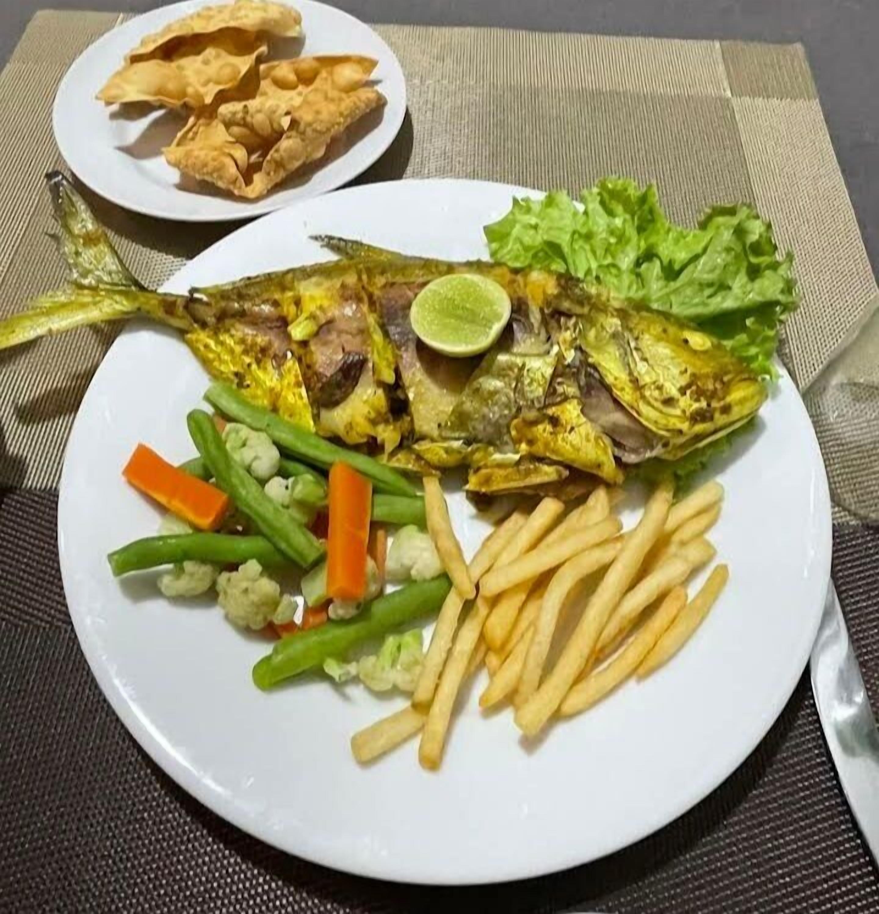 Um prato com peixe grelhado, batatas fritas, legumes e batata palha.