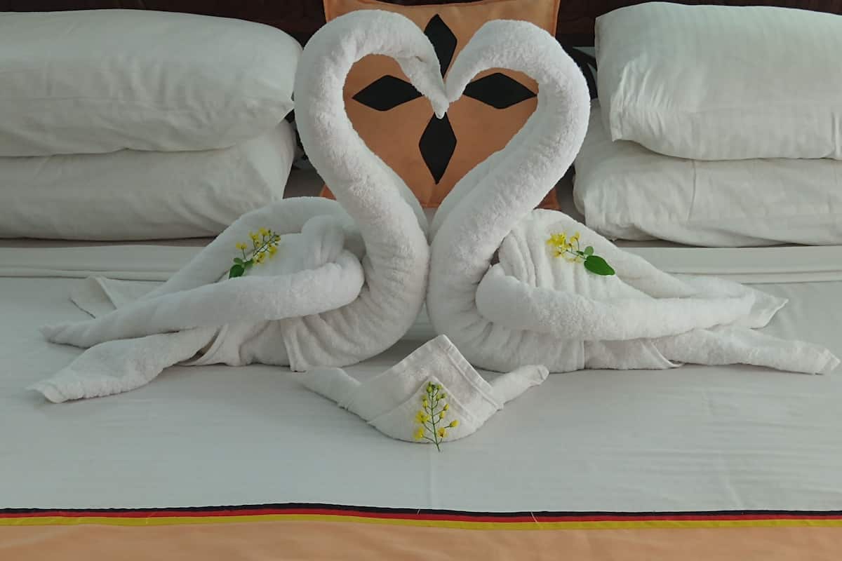 Cama com lençóis brancos e duas toalhas dispostas em formato de cisnes, decoradas com flores.