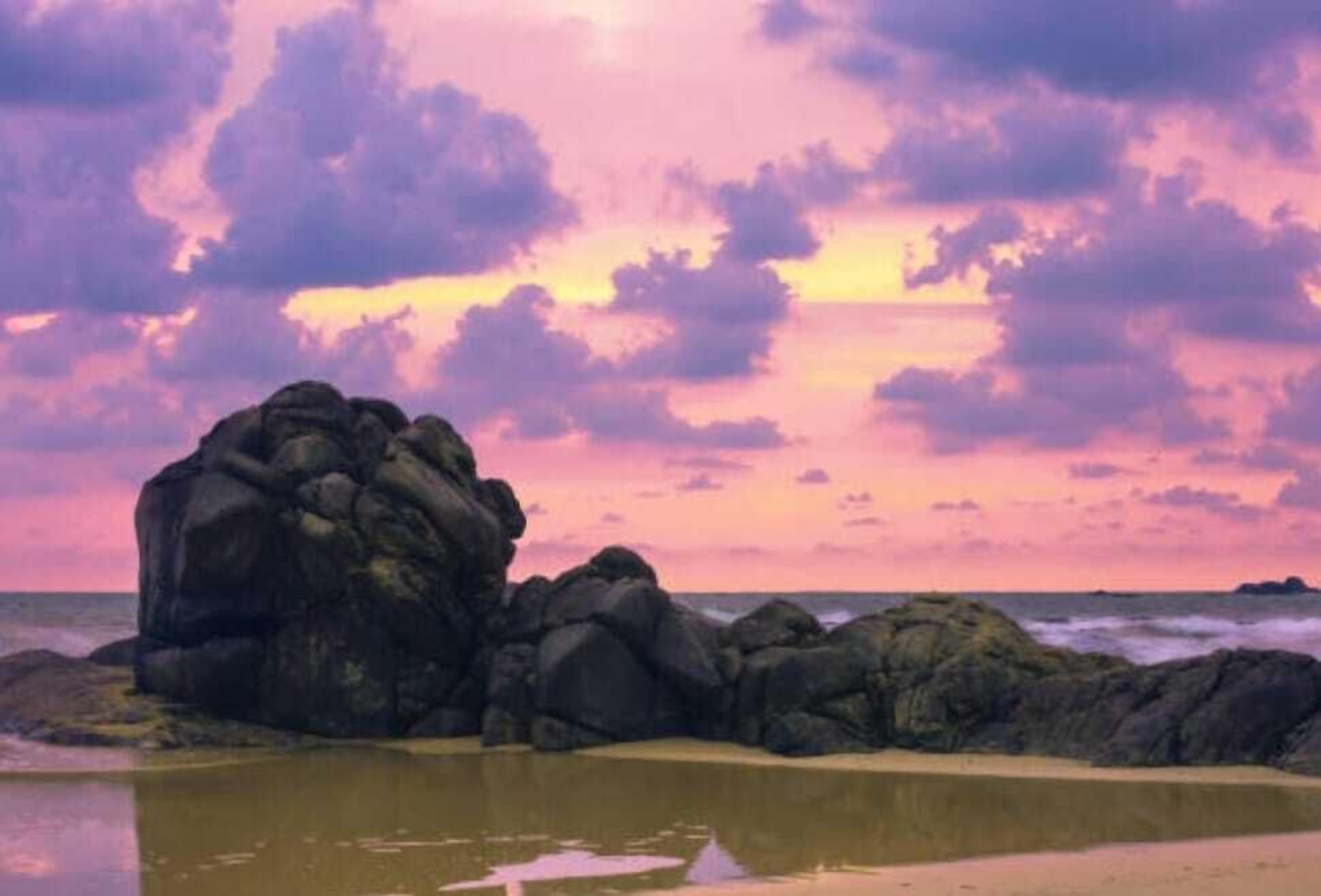 Un paysage côtier avec de gros rochers et une mer calme, sous un ciel au coucher du soleil.