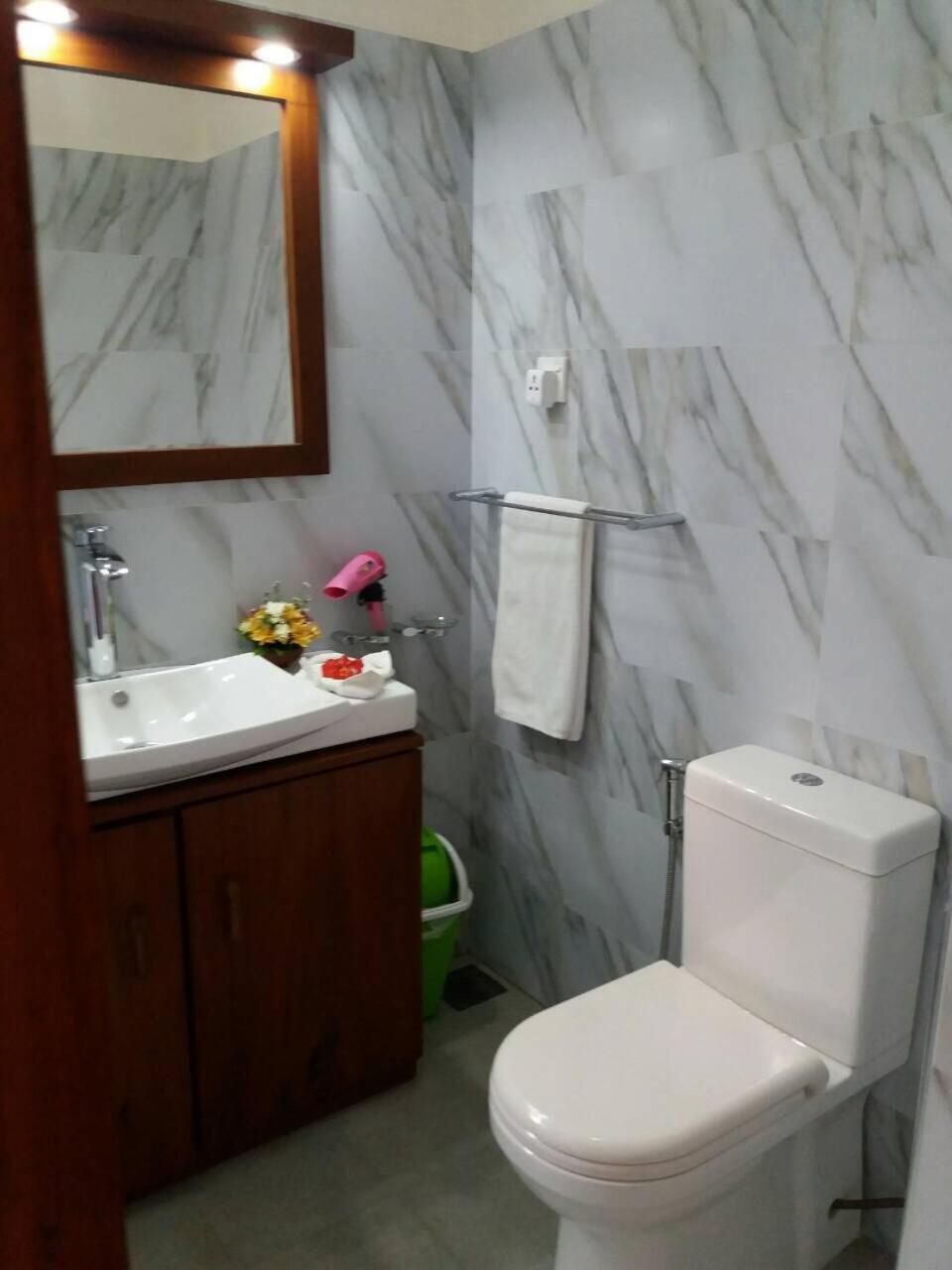 Un baño con pared de mármol, lavabo blanco, inodoro y espejo.