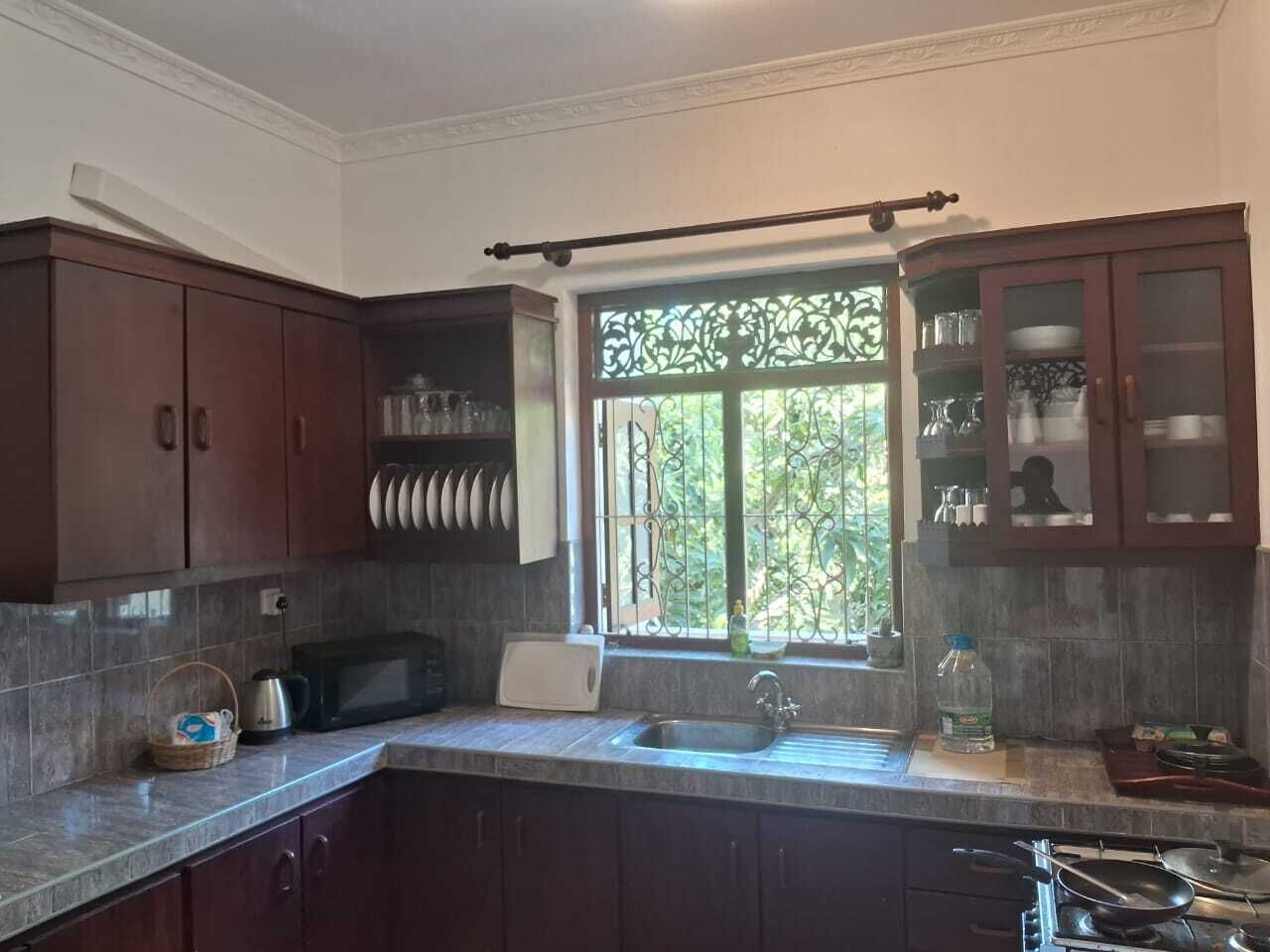 Una cocina con armarios de madera oscura, un lavamanos de acero inoxidable y una ventana con rejas de hierro decorativas.